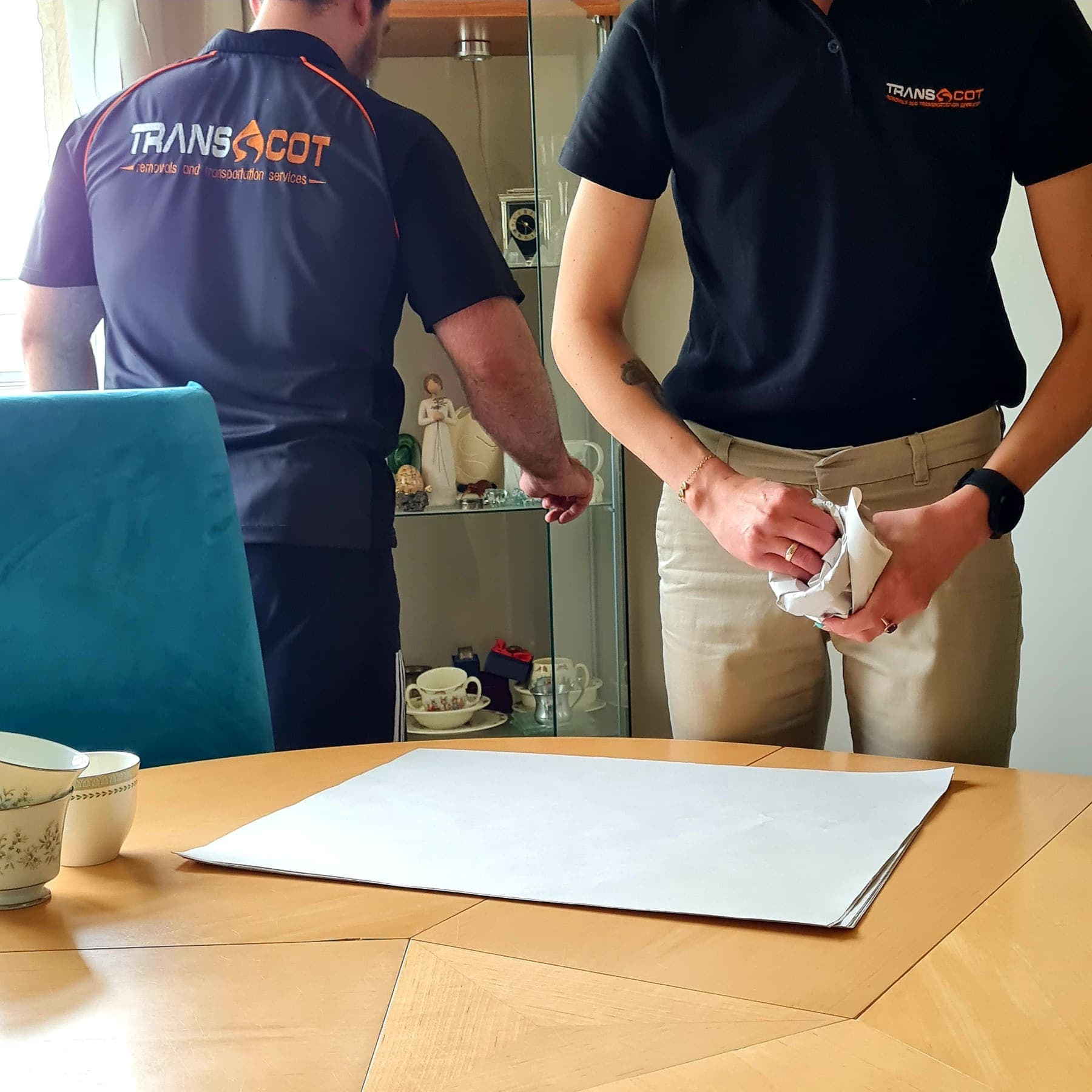 TransScot crew in branded uniform wrapping fragile items at a dining table