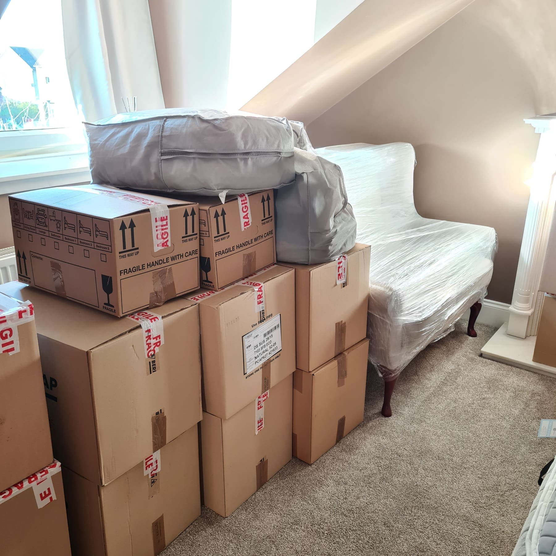 A bedroom packed into labelled TransScot boxes, with a sofa wrapped and protected